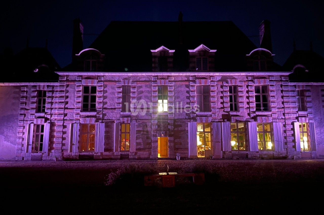 Façade d'un bâtiment ancien éclairée par des lumières violettes et jaunes dans l'obscurité.