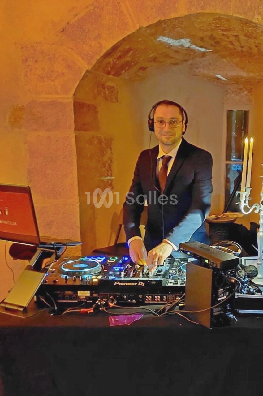 Un DJ en costume mixe de la musique sur une table de mixage dans un cadre en pierre éclairé chaleureusement.