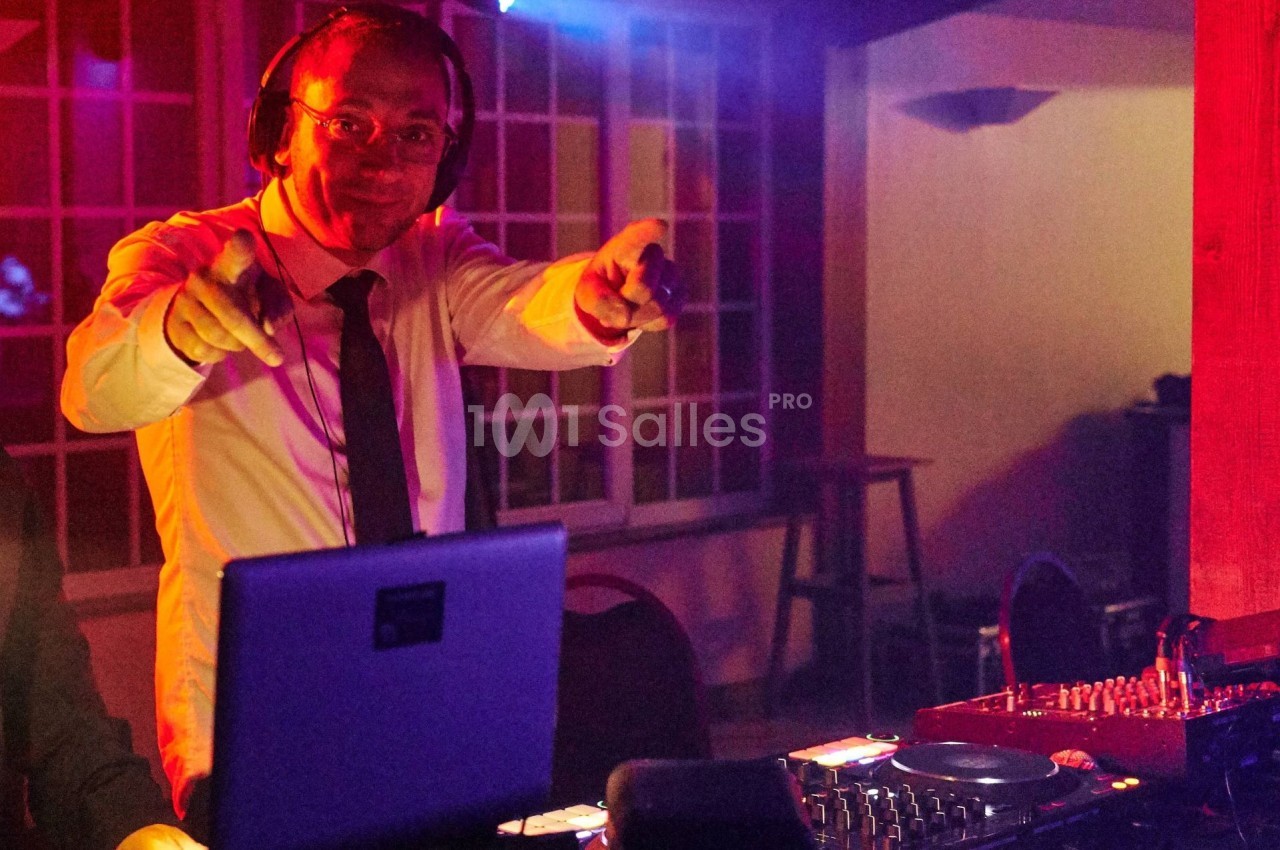 Un DJ en chemise et cravate mixe de la musique sur une table de mixage dans une ambiance lumineuse rouge et violette.