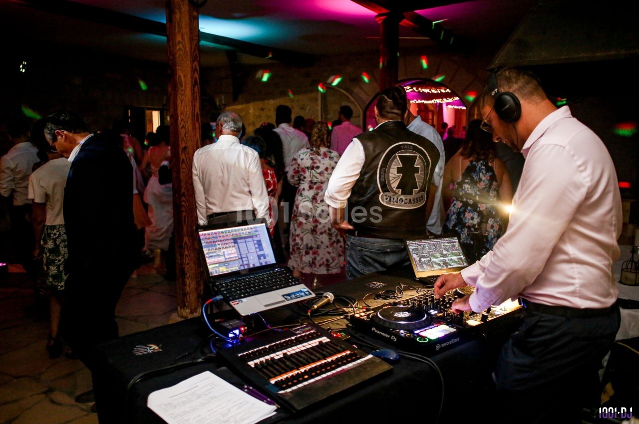 Un DJ mixe de la musique sur une console lors d'une soirée dansante avec des invités sur une piste éclairée.