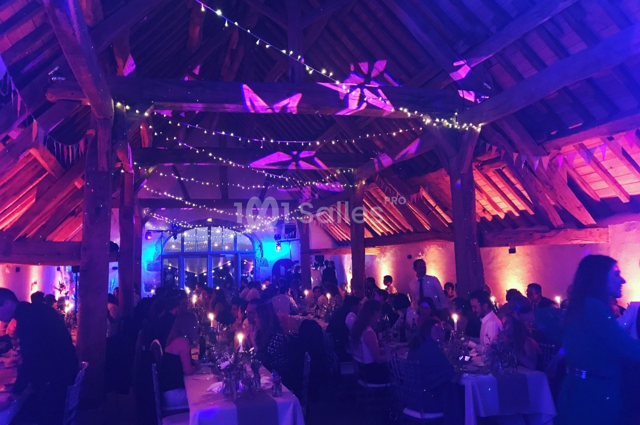 Salle de réception en soirée avec invités attablés, éclairage tamisé et guirlandes lumineuses suspendues.