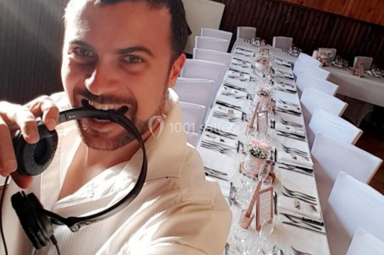 Un homme souriant tenant un casque audio dans une salle décorée avec une longue table dressée pour un événement.