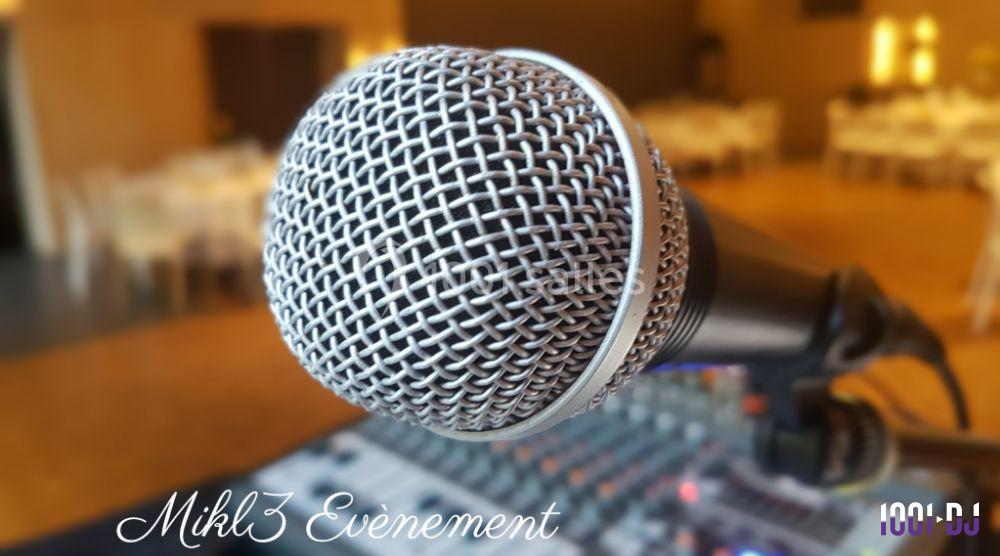 Microphone en gros plan devant une table de mixage, avec une salle floutée en arrière-plan.