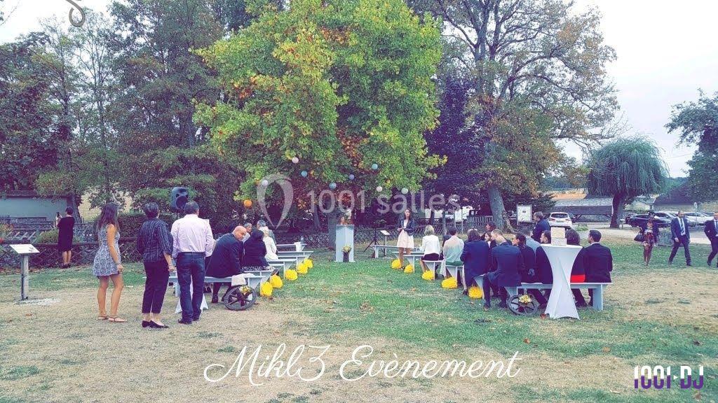 Cérémonie en plein air avec invités assis, décorations jaunes et un arbre central dans un cadre verdoyant.