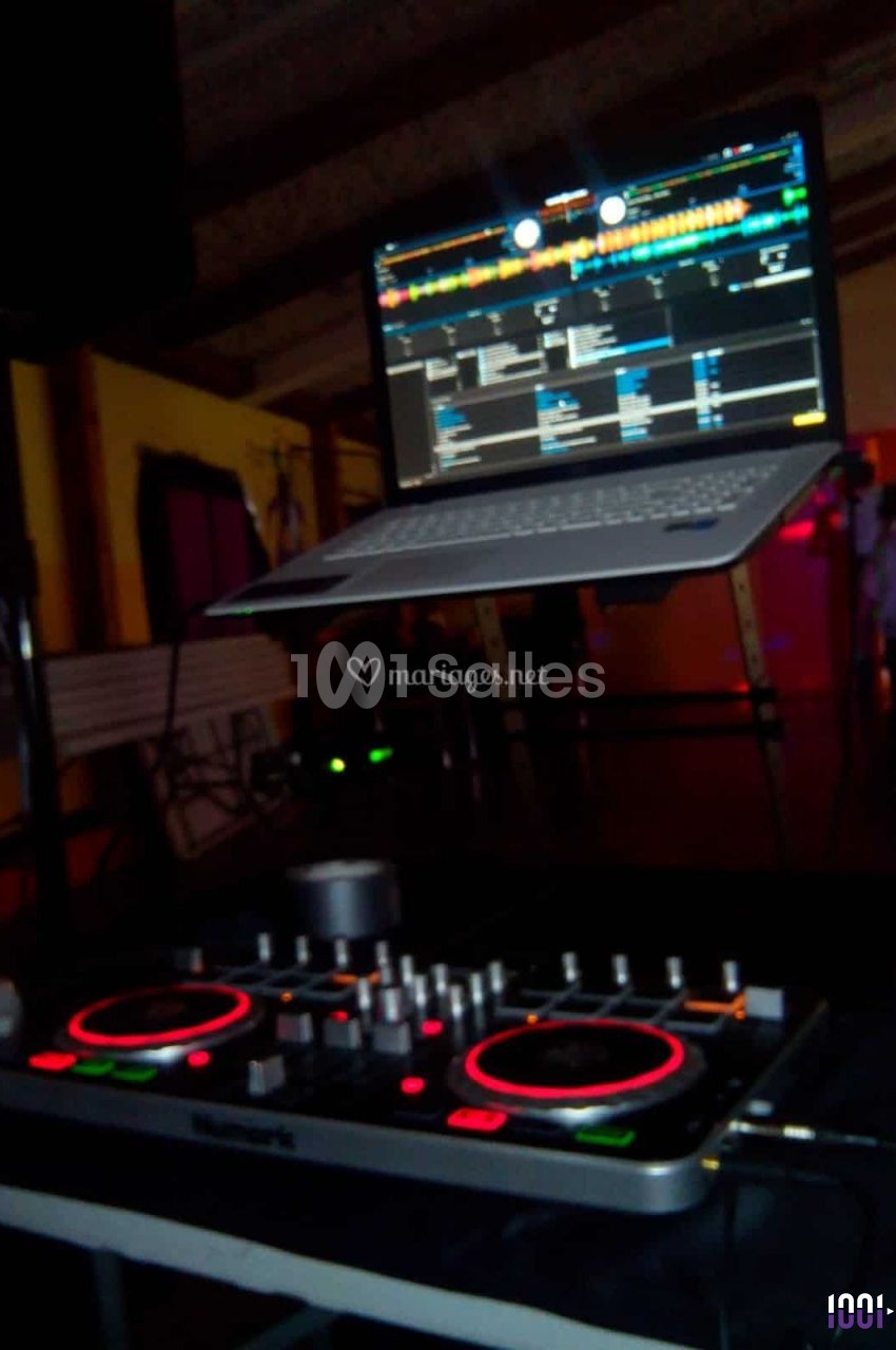 Console de mixage DJ avec un ordinateur portable affichant un logiciel de musique, dans un environnement sombre.