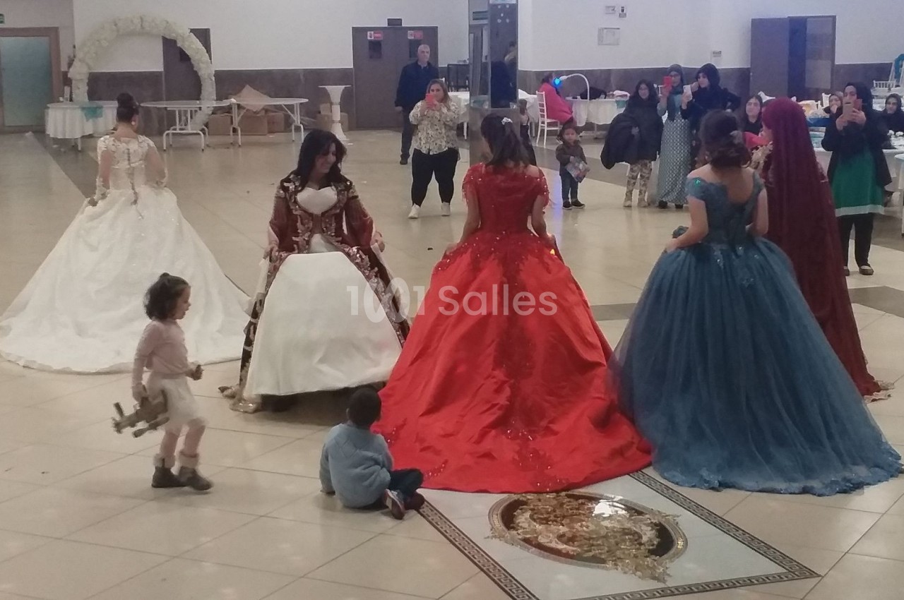Des femmes en robes de soirée colorées discutent dans une grande salle avec des enfants assis au sol.