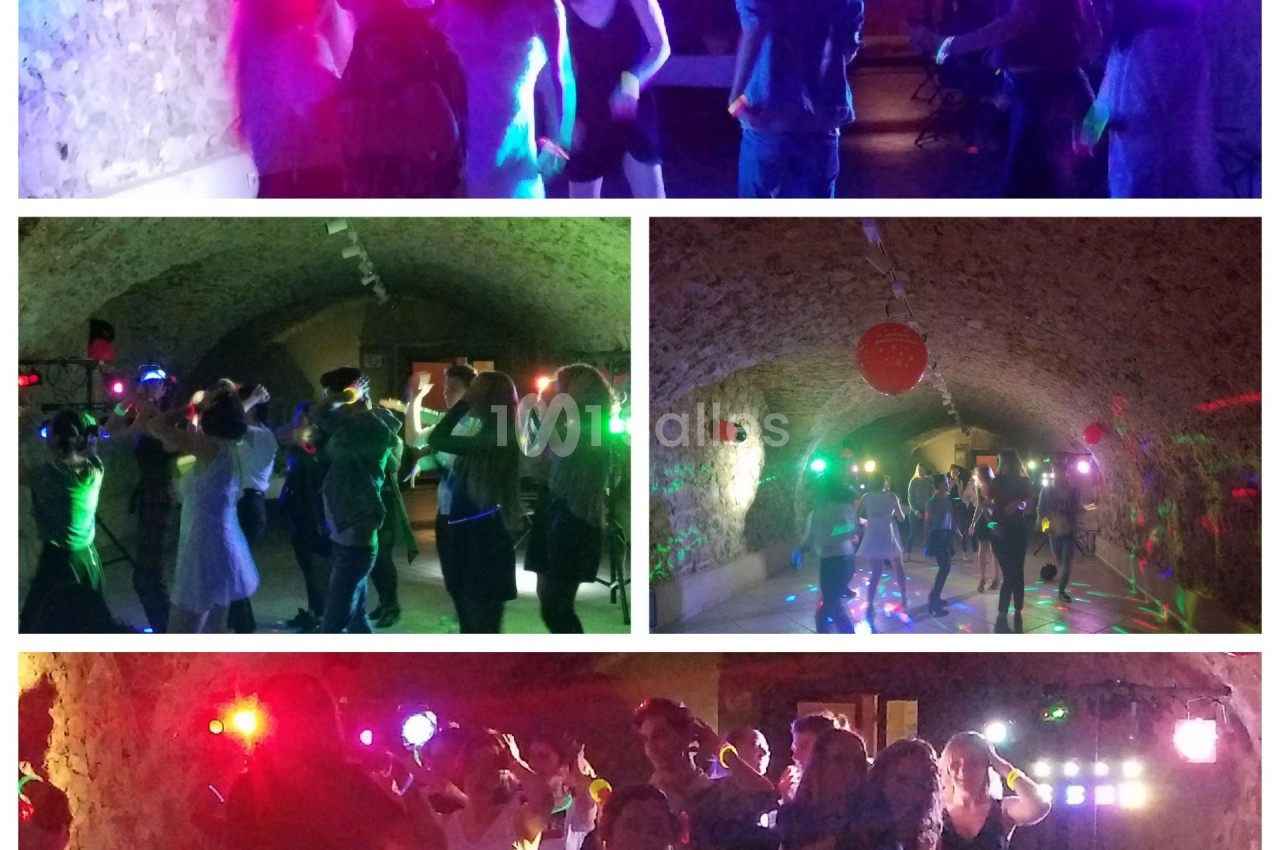 Personnes dansant sous des lumières colorées dans une salle voûtée en pierre.