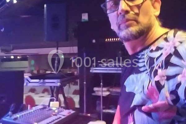 Un homme devant une console de mixage dans une salle équipée de matériel audio et éclairée par des lumières tamisées.