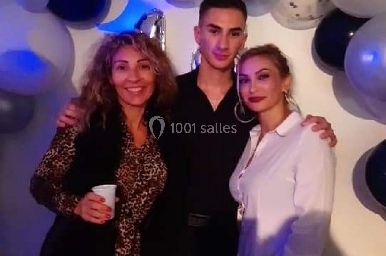 Trois personnes posent devant une décoration murale composée de ballons noirs, blancs et argentés.