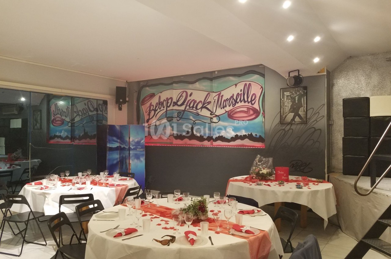 Salle décorée pour un événement avec des tables dressées, des nappes blanches et une fresque murale ’Bébé Rock Marseille’.