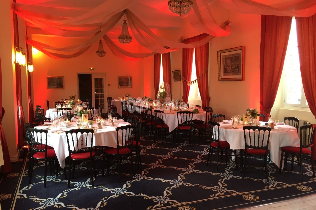 Salle de réception décorée avec des tables dressées, des chaises noires et rouges, et un éclairage rouge chaleureux.