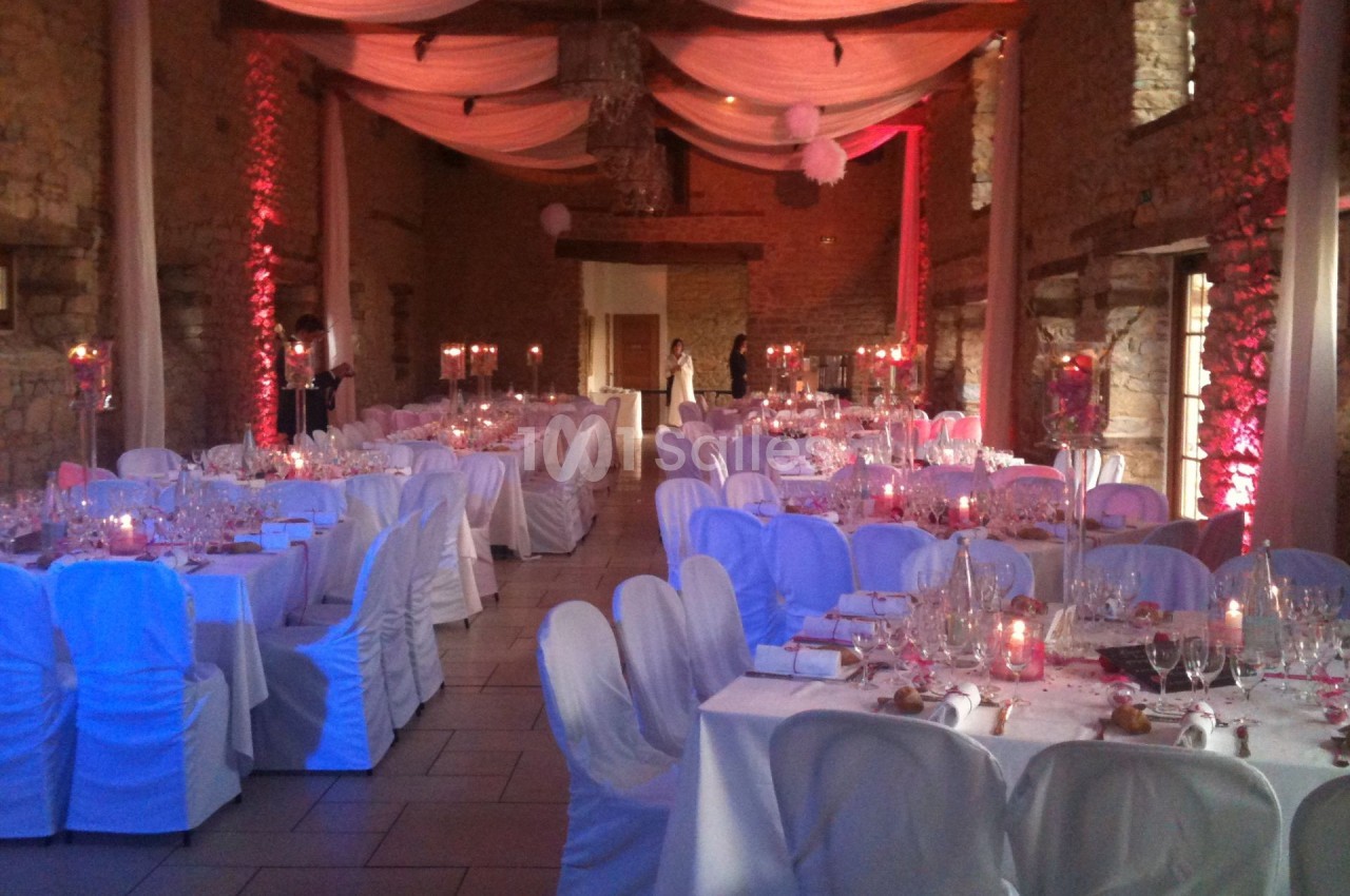 Salle de réception décorée pour un mariage, avec tables dressées, chaises blanches et éclairage tamisé.