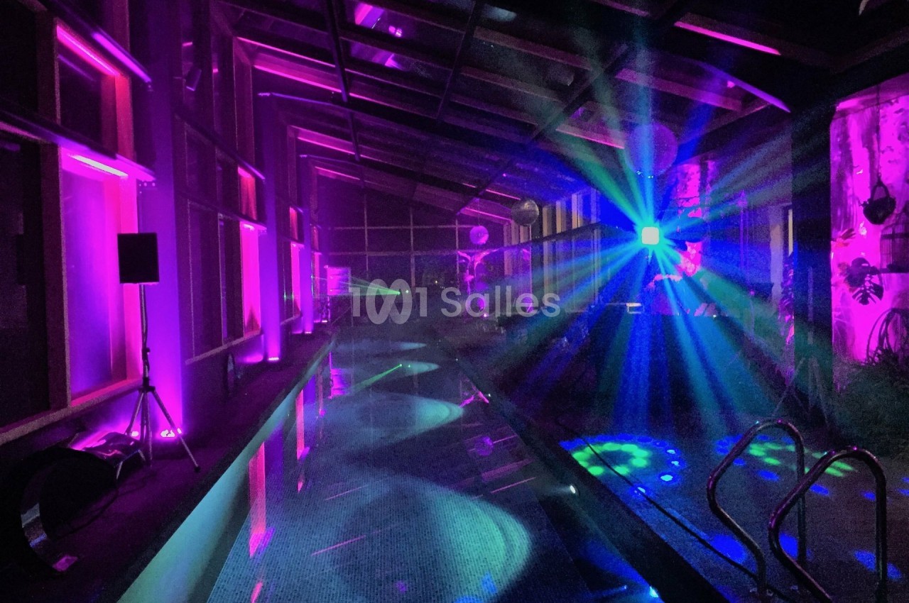 Piscine intérieure éclairée par des lumières colorées et des effets lumineux dans une ambiance nocturne.
