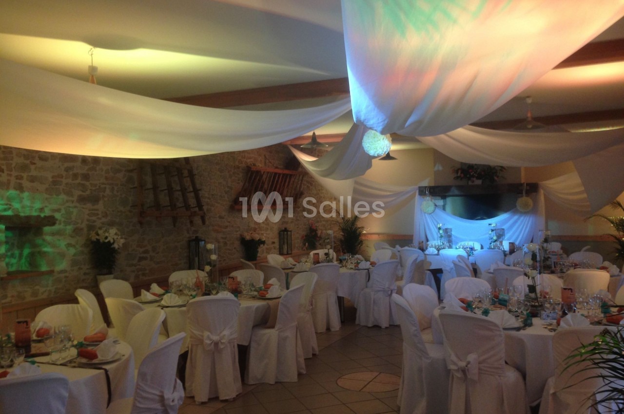 Salle de réception décorée avec des nappes blanches, des tables dressées et un éclairage coloré.