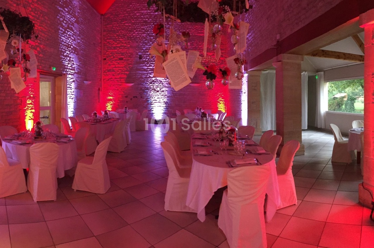 Salle en pierres apparentes décorée pour un événement, avec tables dressées et éclairage rouge et blanc.