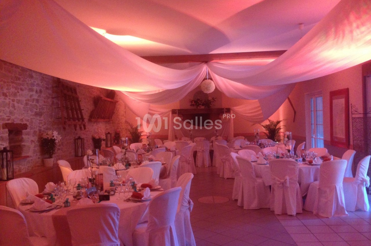 Salle de réception décorée avec des nappes blanches, des tables dressées et un éclairage tamisé.