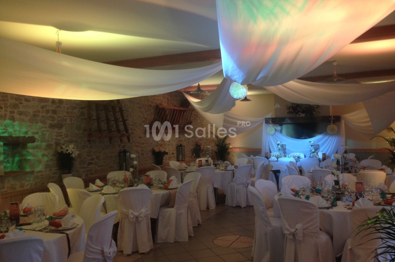 Salle de réception décorée avec des voilages blancs, des tables dressées et des chaises couvertes de housses.