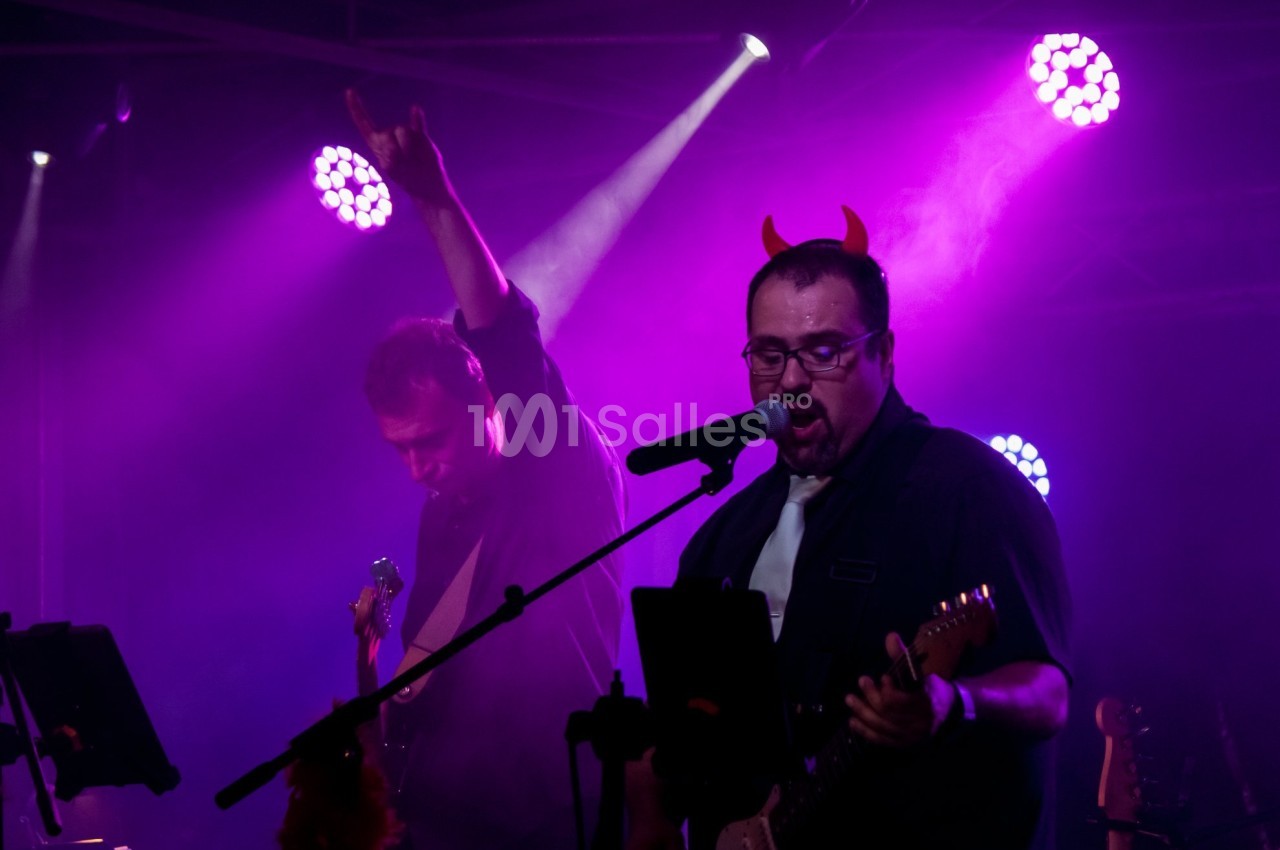 Deux musiciens sur scène sous des lumières violettes, l'un portant des cornes rouges et chantant au micro.