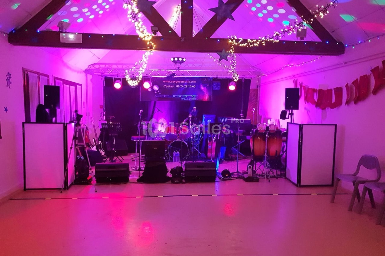 Salle décorée avec guirlandes lumineuses, scène équipée de matériel musical et éclairages colorés.