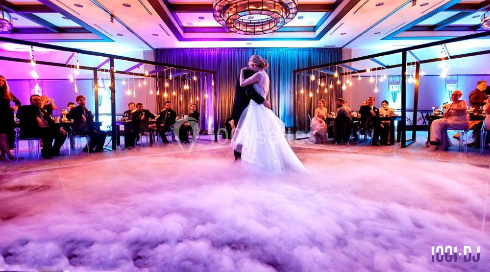 Un couple danse au centre d'une salle de réception éclairée, entouré de fumée et d'invités assis.