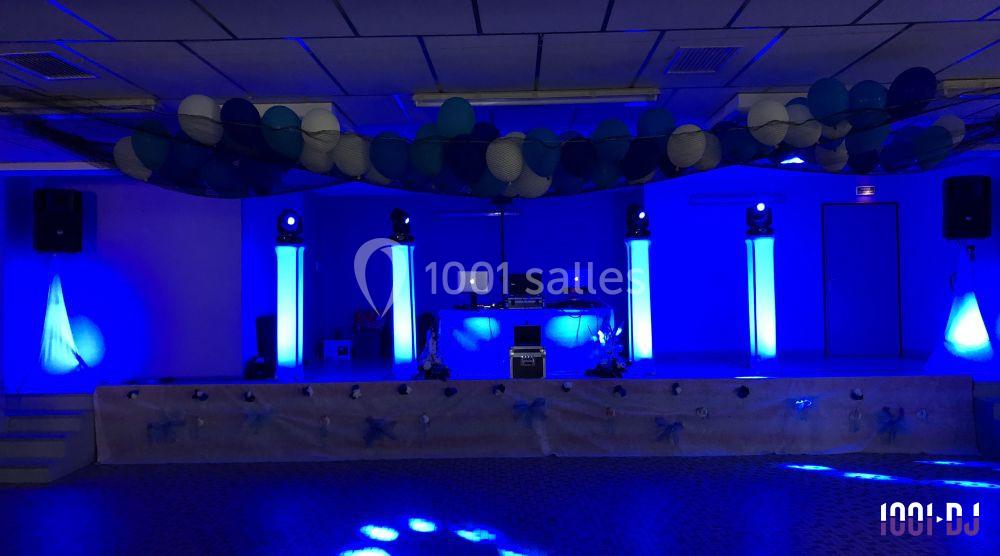 Salle décorée en bleu avec des ballons suspendus, un espace DJ éclairé et des colonnes lumineuses.