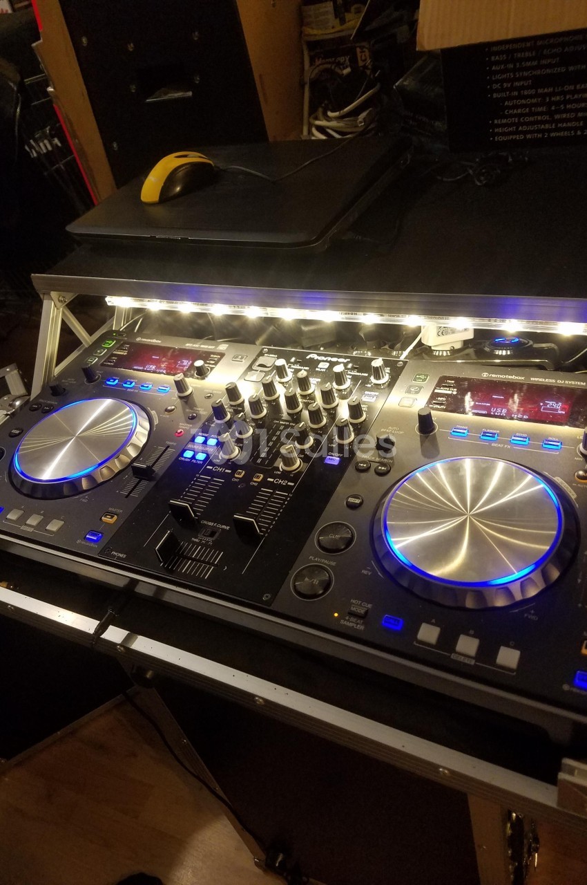 Table de mixage DJ avec platines, boutons et éclairage LED, posée sur un support dans un environnement intérieur.