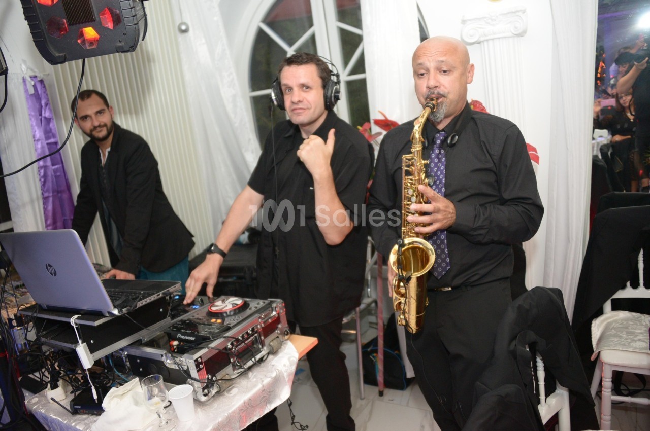 Un DJ mixe de la musique tandis qu'un saxophoniste joue devant un public dans une salle éclairée.