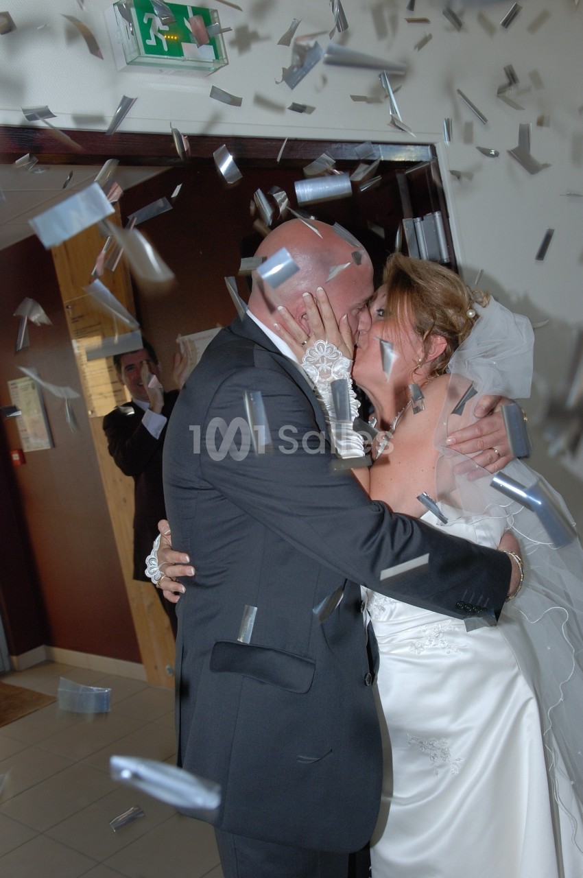 Un couple en tenue de mariage s'embrasse sous une pluie de confettis dans un intérieur festif.