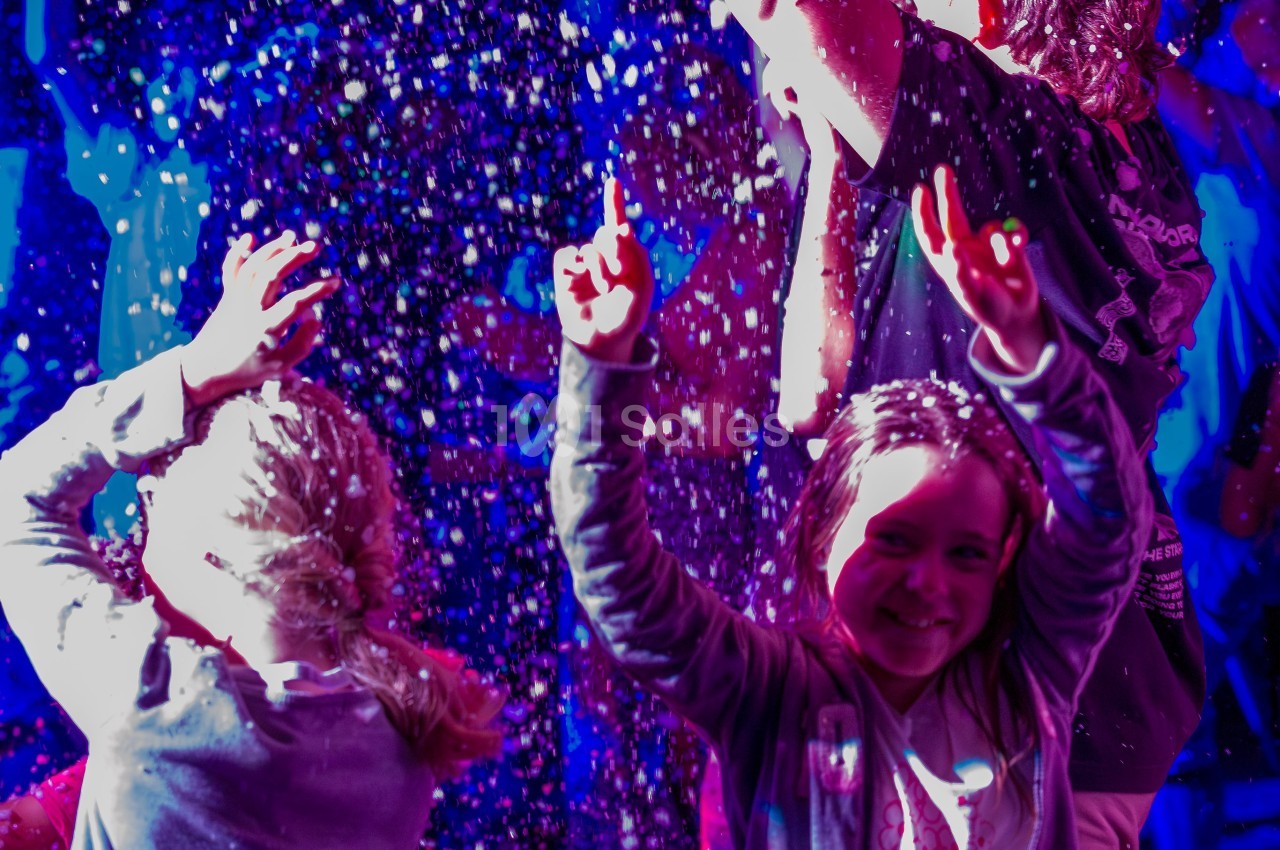 Des enfants souriants jouent sous une pluie de confettis lumineux dans une ambiance festive et colorée.
