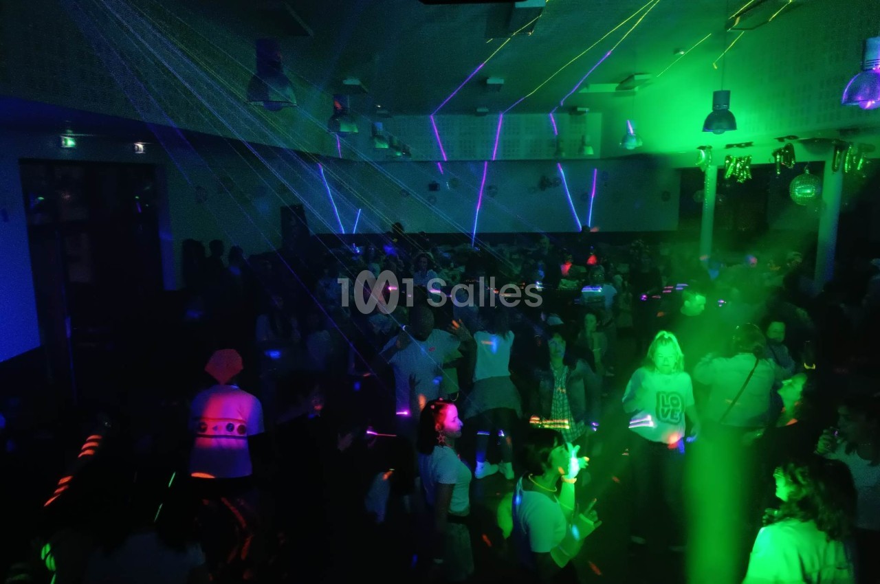 Des personnes dansent dans une salle sombre éclairée par des lumières laser vertes et violettes.