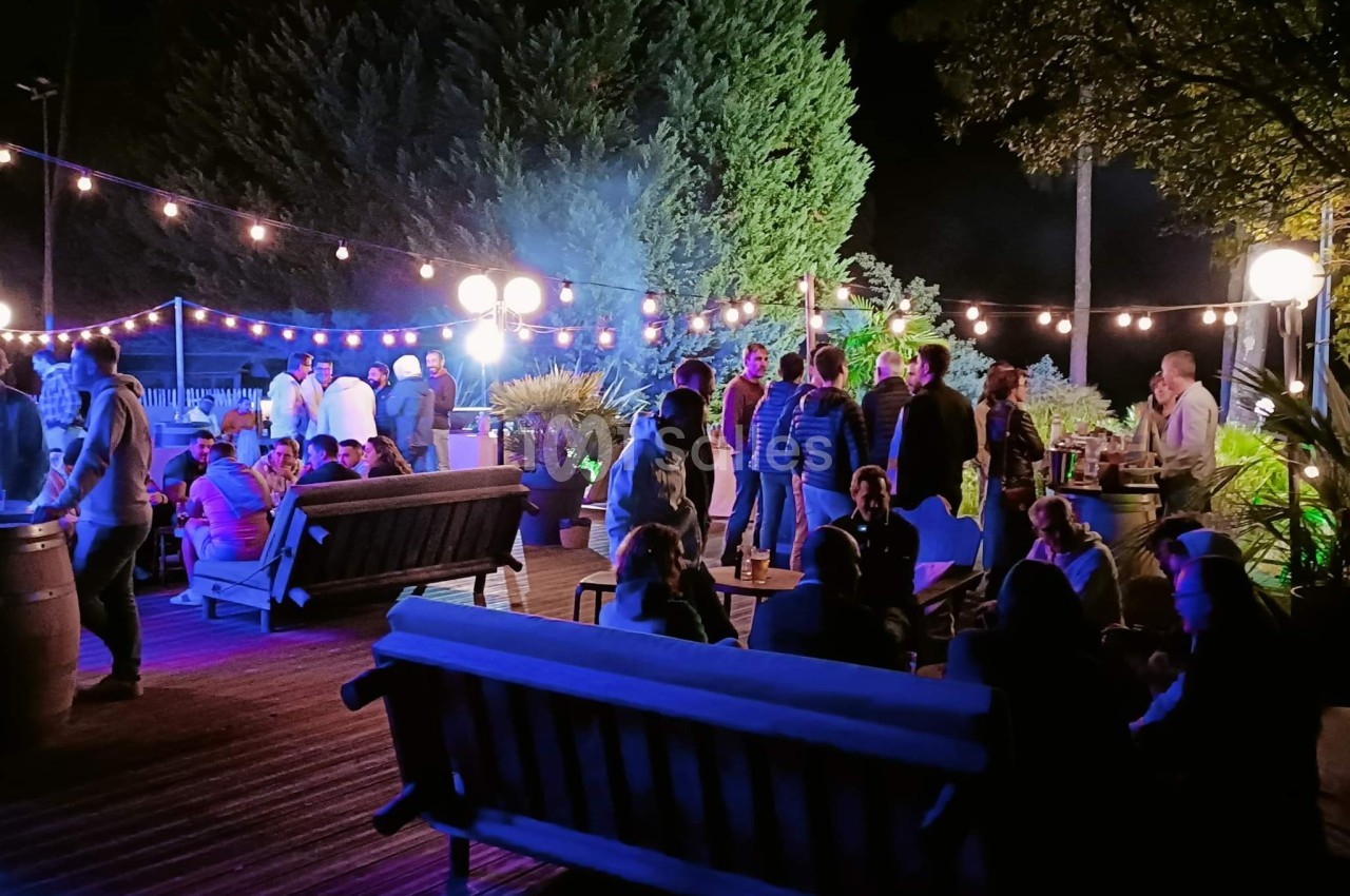 Groupe de personnes réunies en soirée en plein air, éclairées par des guirlandes lumineuses et des lampadaires.