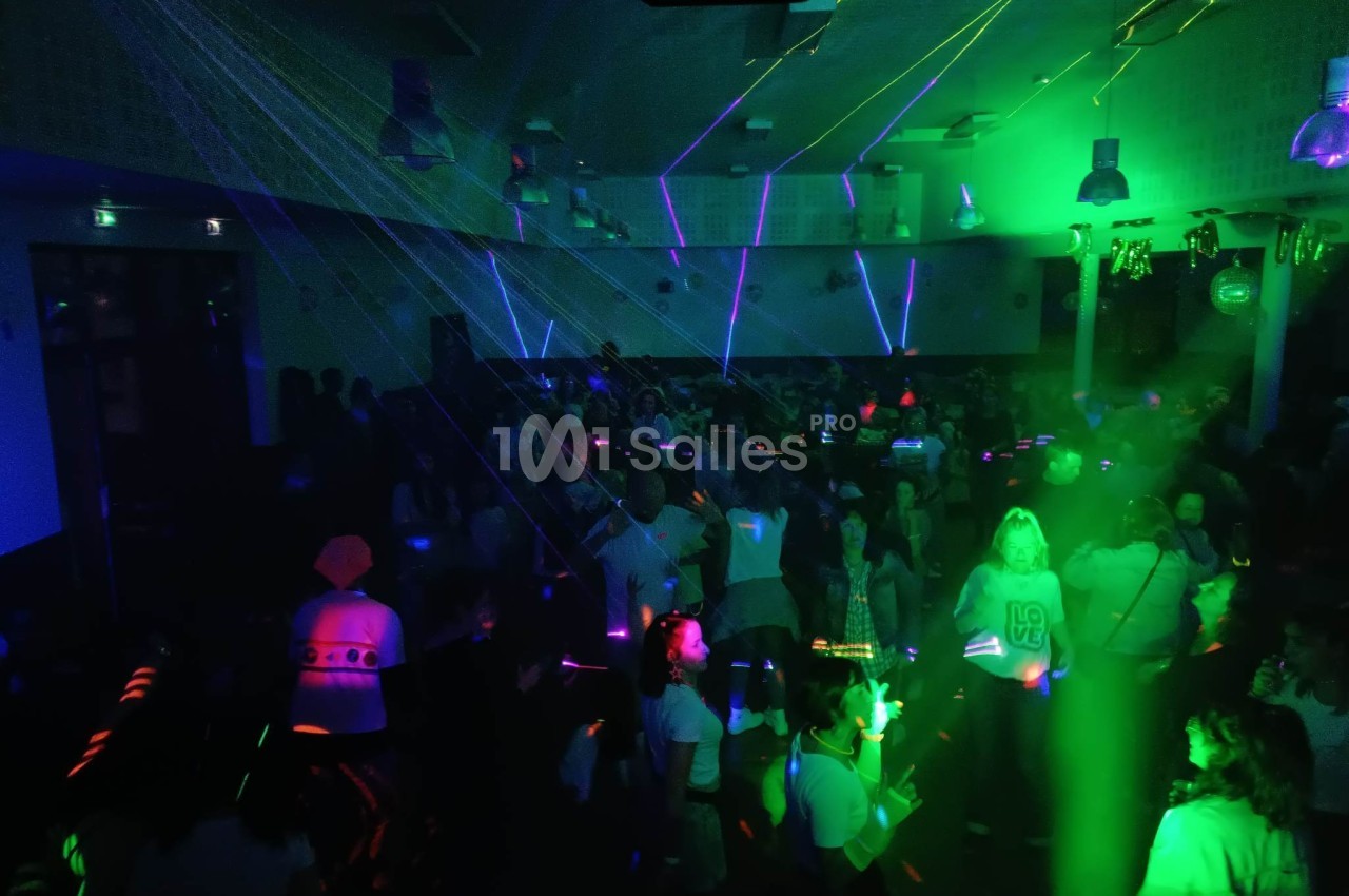 Des personnes dansent dans une salle sombre éclairée par des lumières laser vertes et violettes.