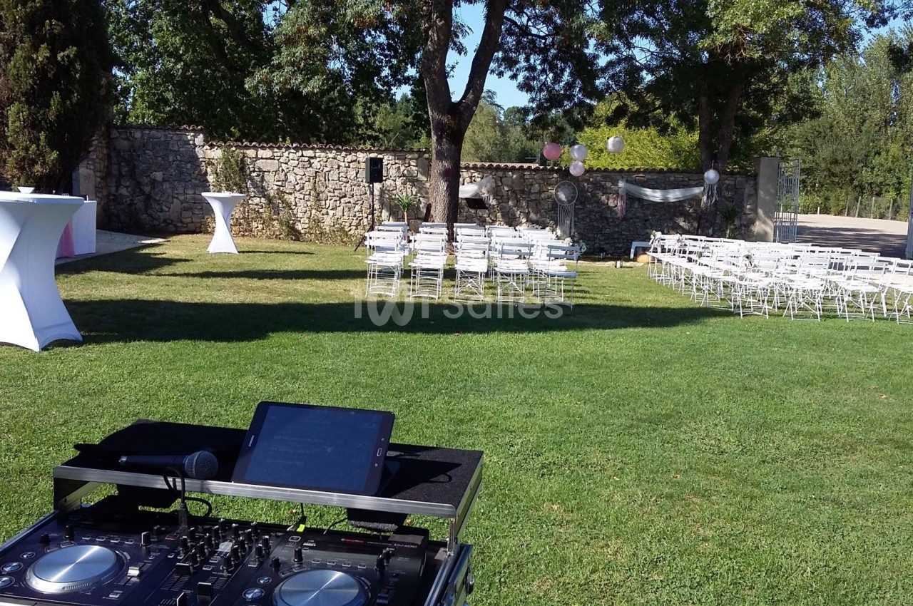Installation d'une table de mixage en extérieur avec des chaises blanches disposées pour un événement dans un jardin.