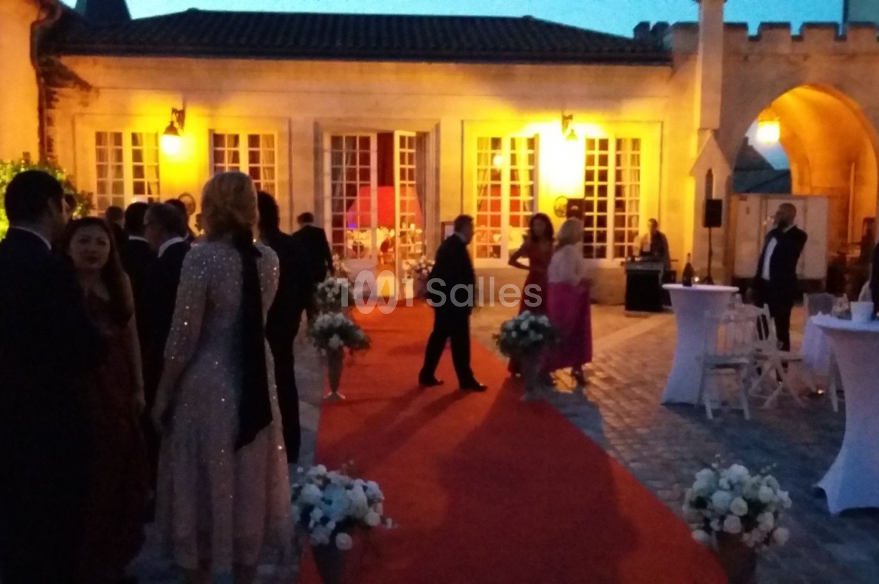 Personnes en tenue de soirée discutant sur un tapis rouge dans une cour éclairée au crépuscule.