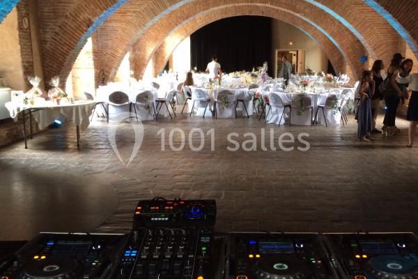 Salle voûtée en briques avec tables décorées pour un événement, vue depuis une régie DJ au premier plan.
