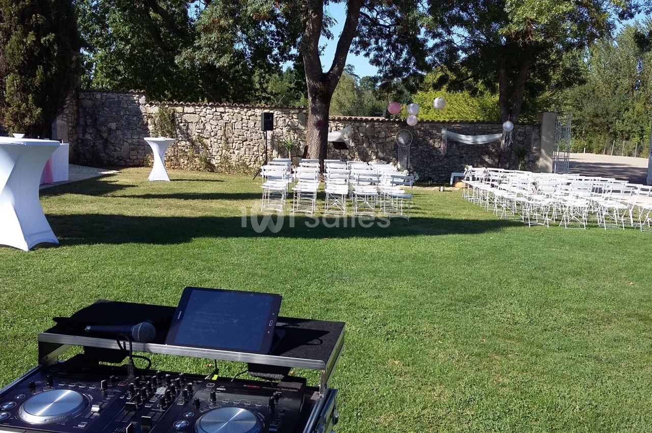 Installation d'une table de mixage en extérieur avec des chaises blanches disposées pour un événement dans un jardin.