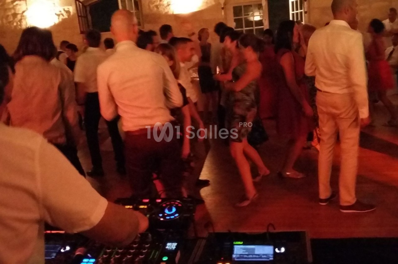 Des personnes dansent dans une salle éclairée de lumières chaudes, avec une table de mixage visible au premier plan.