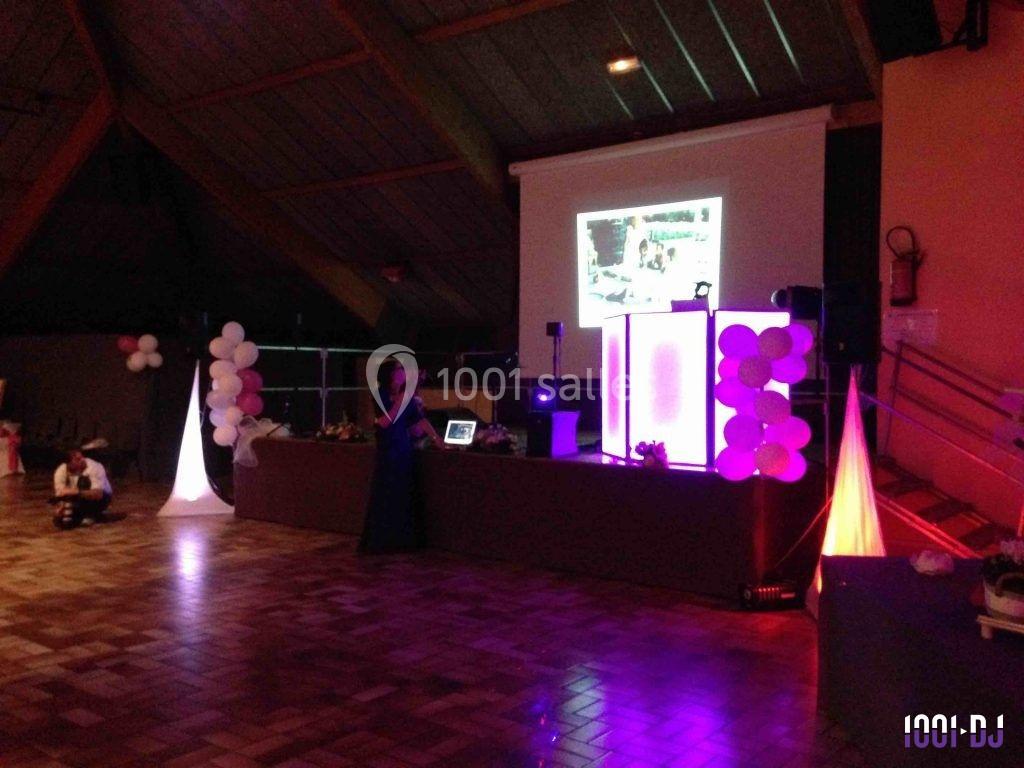 Salle de réception avec éclairage coloré, écran de projection, table de DJ et décoration festive.