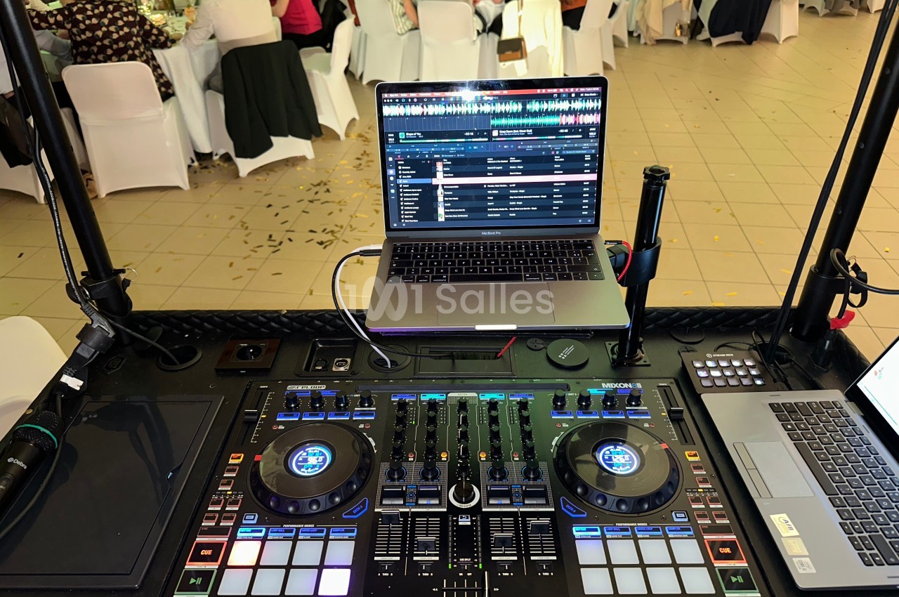 Poste de DJ avec une console de mixage, un ordinateur portable et un micro, dans une salle de réception animée.