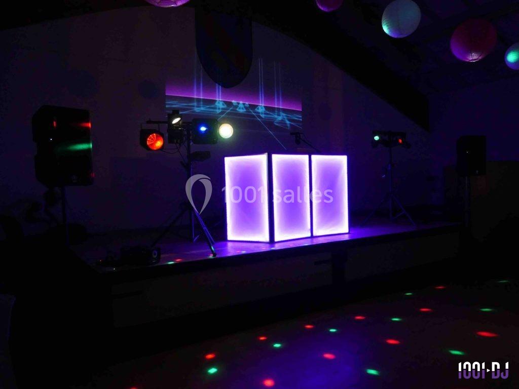 Console de DJ éclairée en violet, entourée de projecteurs colorés et d'effets lumineux dans une salle sombre.