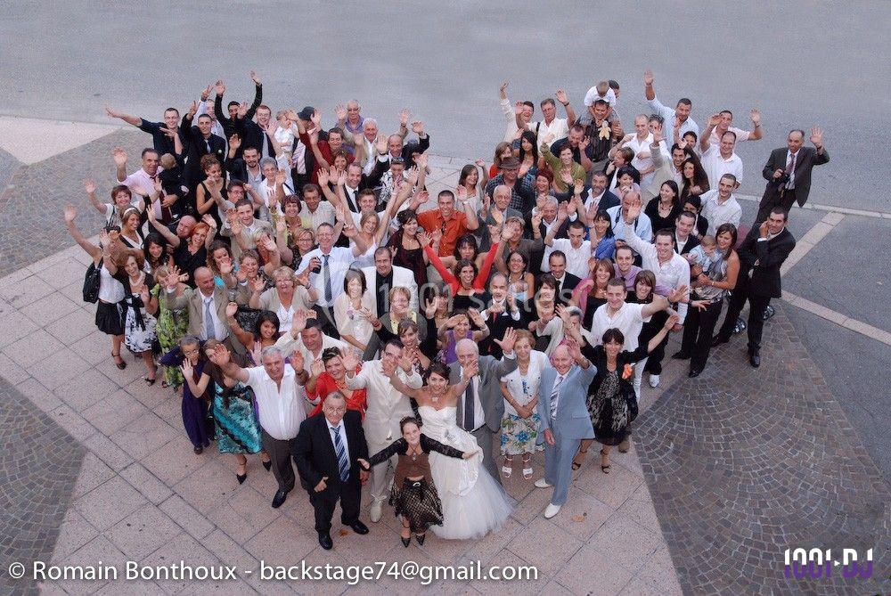 Un grand groupe de personnes posant joyeusement pour une photo de groupe en extérieur, vu en plongée.