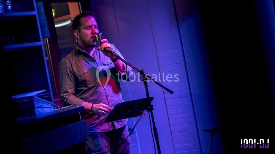 Un homme chante au micro sur une scène éclairée par des lumières bleues et violettes.