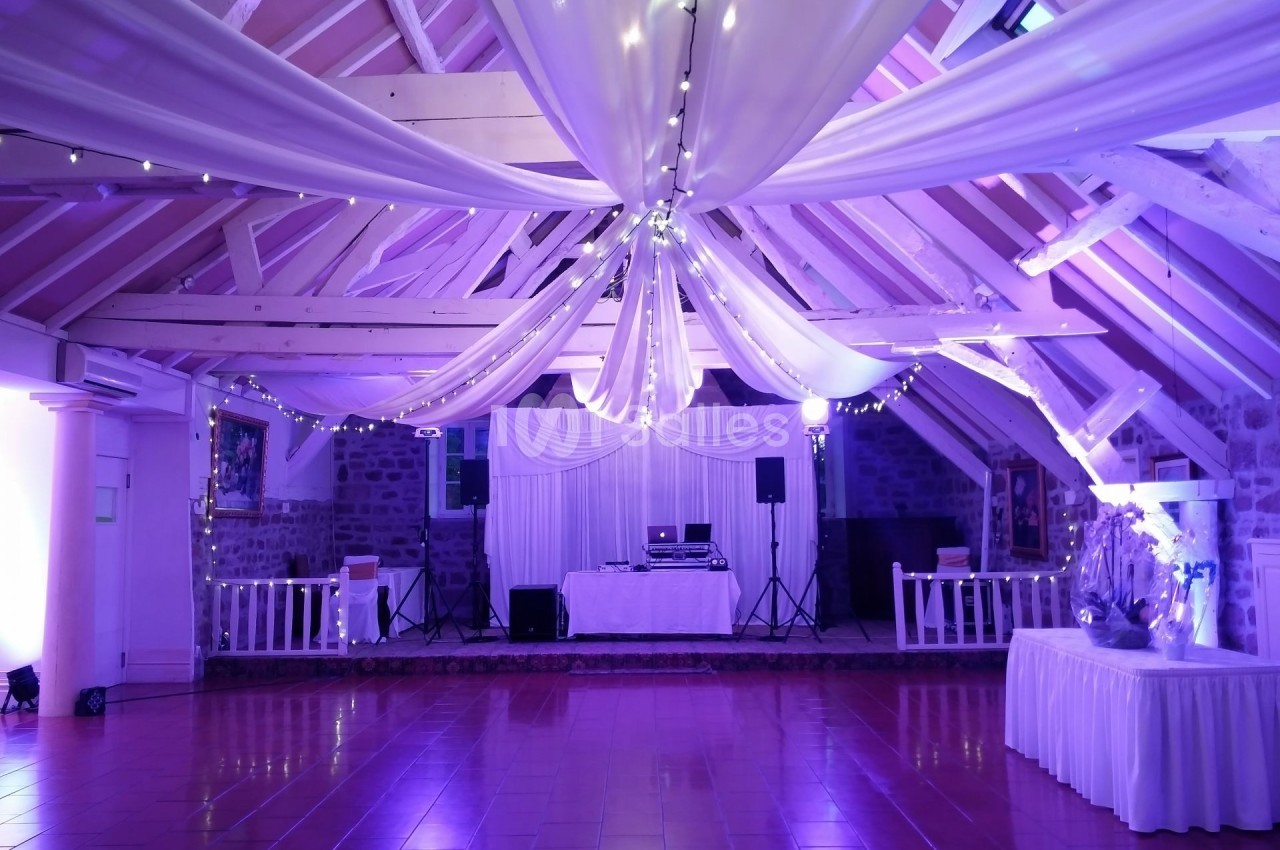 Salle de réception avec charpente apparente, éclairage violet, décorations en tissu et équipements de sonorisation.