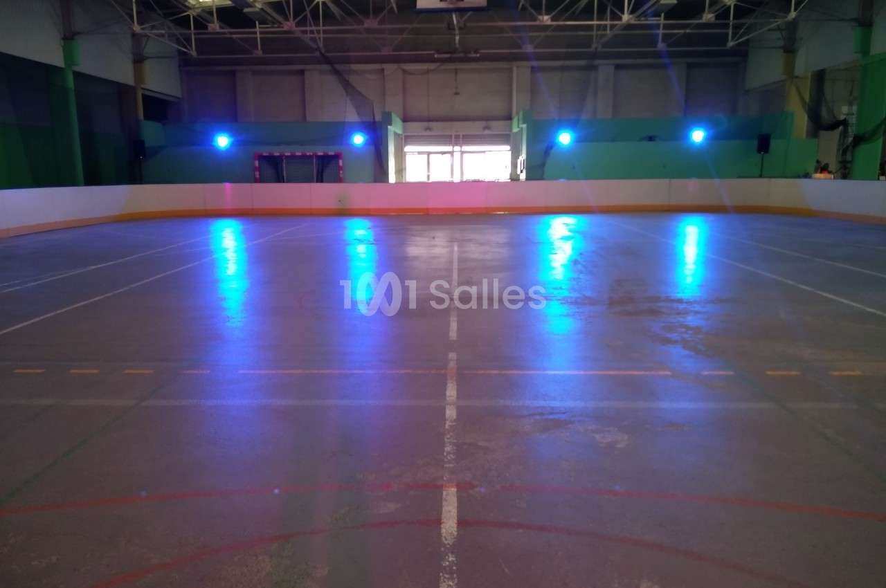 Patinoire intérieure vide avec éclairage bleu, lignes marquées au sol et structure métallique visible au plafond.