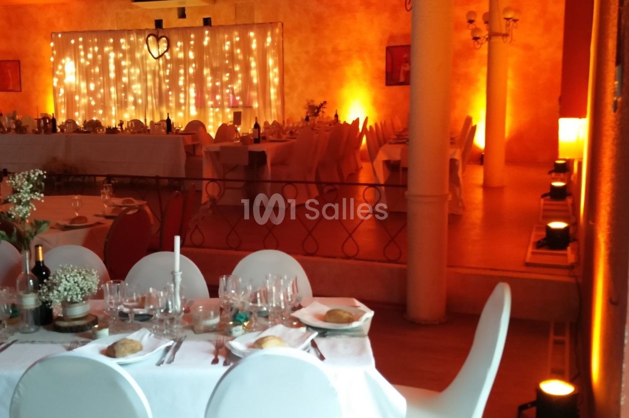 Salle de réception décorée avec des guirlandes lumineuses, tables dressées et ambiance chaleureuse.