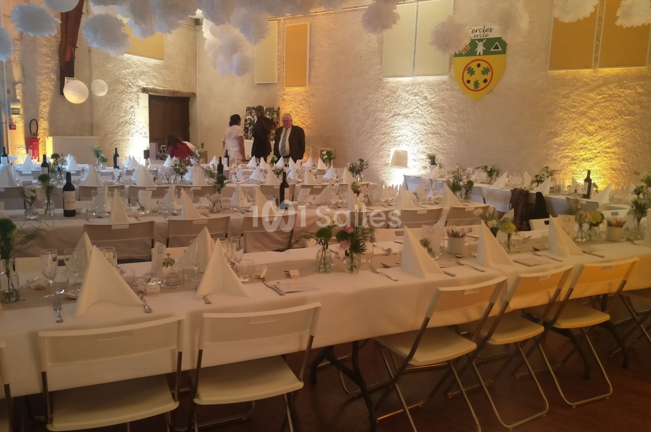 Salle de réception décorée avec des tables dressées, nappes blanches, serviettes pliées et arrangements floraux.