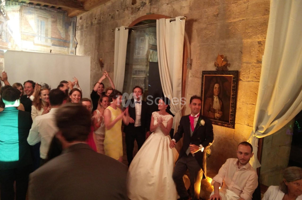 Groupe de personnes célébrant un mariage dans une salle en pierre avec des rideaux blancs et un tableau au mur.