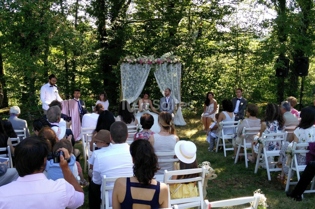 Cérémonie de mariage en plein air avec des invités assis, un couple devant un arche fleuri et un officiant.