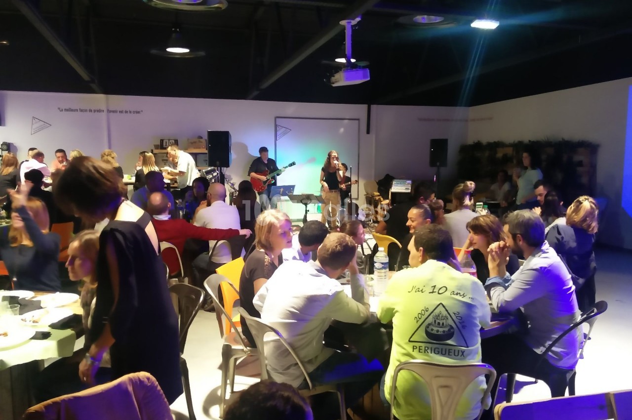 Des personnes dînent et discutent dans une salle animée avec un groupe de musique jouant en arrière-plan.