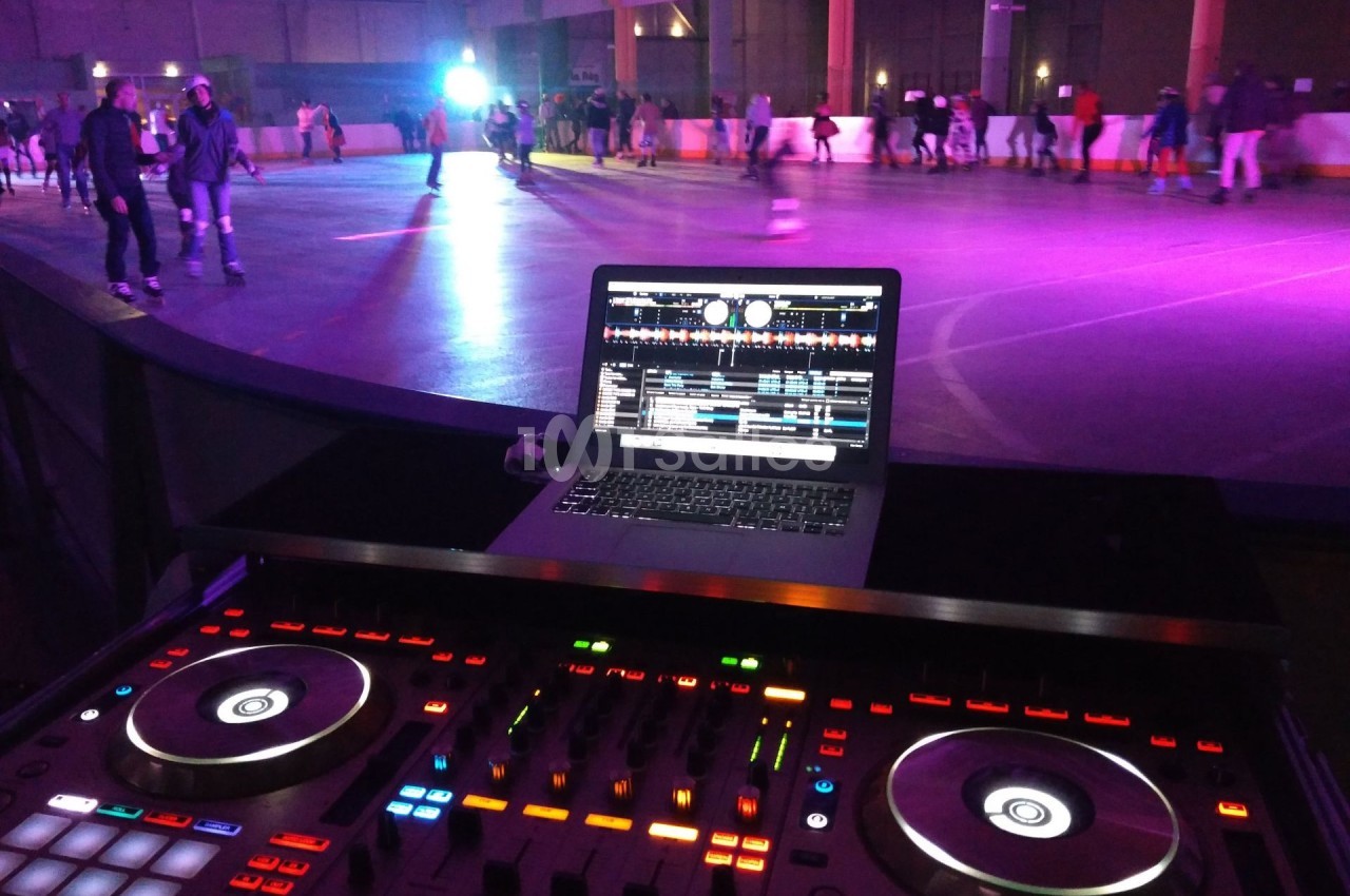 Table de mixage et ordinateur portable affichant un logiciel DJ, avec une piste de roller éclairée en arrière-plan.